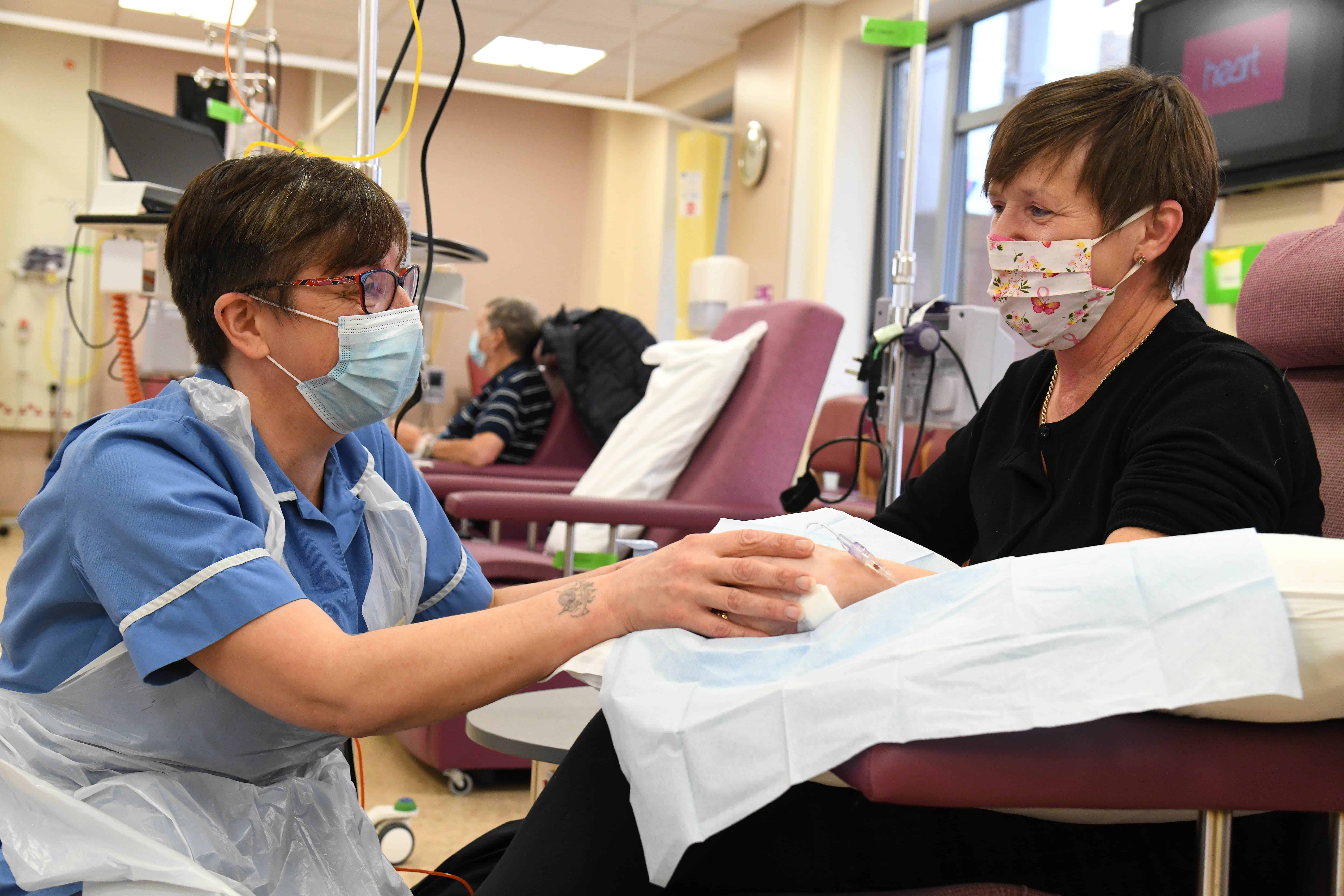 Picture of someone receiving treatment in a chair witha nurse holding her hand and knelt down next to her