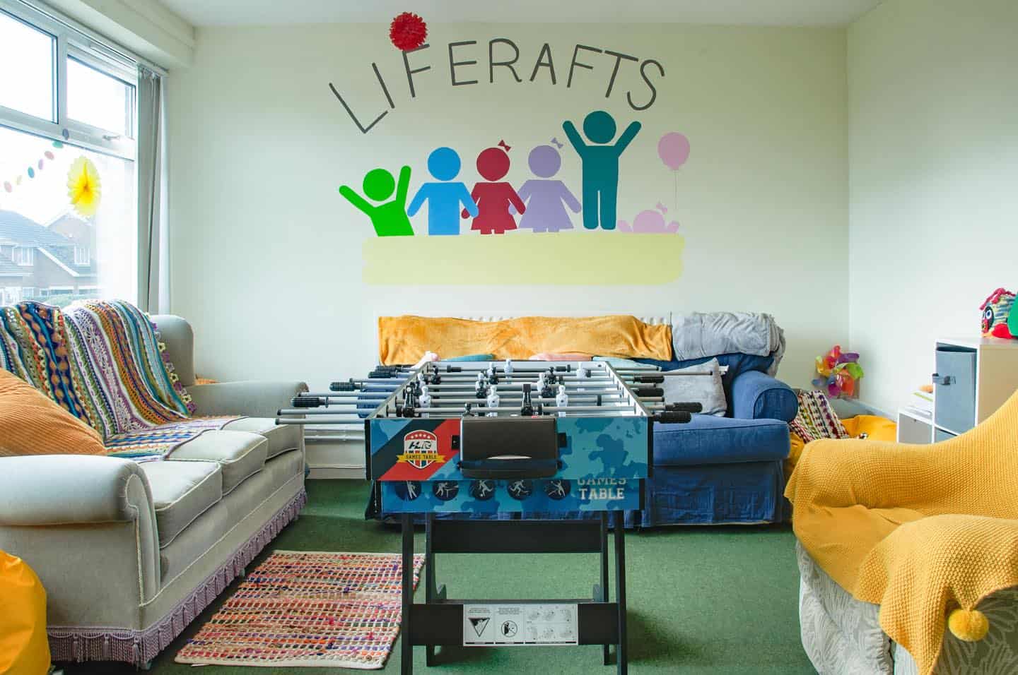 A colourful room used to host a support group for children whose family members have or have had cancer. There's a table football table in the middle of the room and it's surrounded by comfortable sofas, colourful rugs and toys for children of all ages.