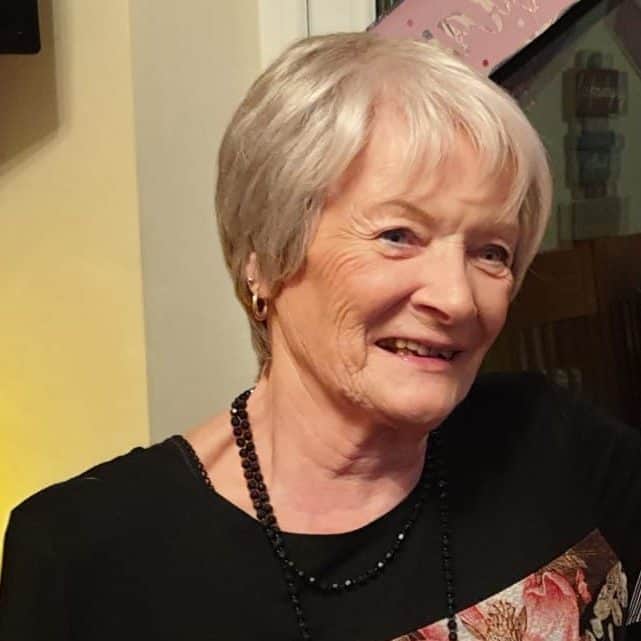 Headshot of Margaret Allbones, a cancer survivor who shared her story with us. She is smiling, looking slightly to the right of the camera, and wearing a black jumper. She has cropped blonde hair and is wearing small gold hoop earrings.
