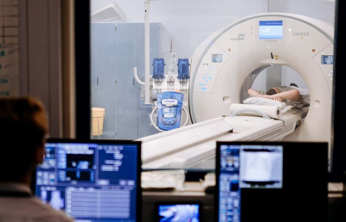Image of CT scanner with someone sat looking at the screens in the booth