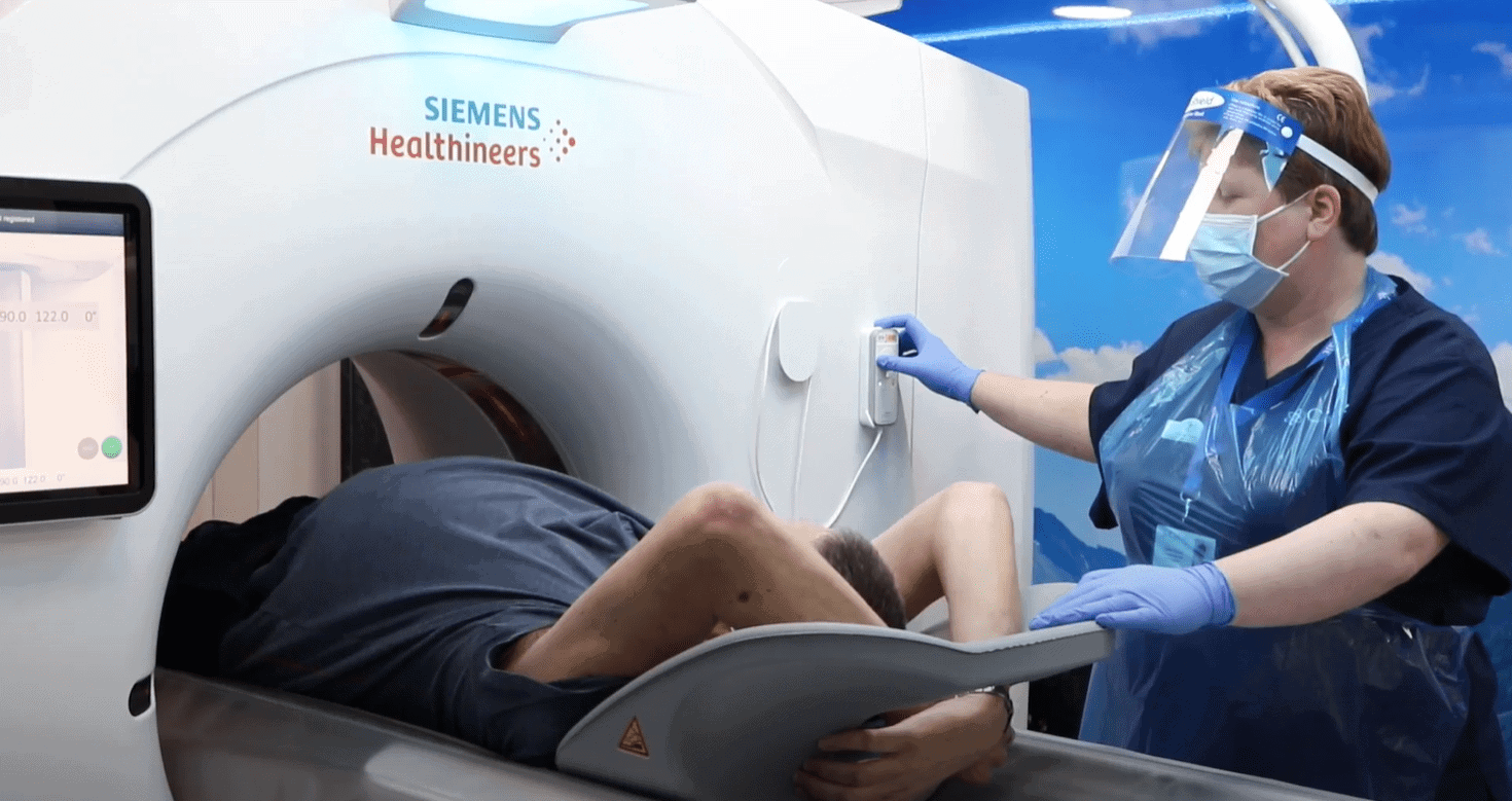 A man receiving a CT scan as part of the Targeted Lung Health Check Programme. A radiographer is pictured next to him, operating the CT scanner.