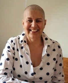 Allyson is looking at the camera and smiling. She is wearing a black and white polka dot blouse and has a shaved head.