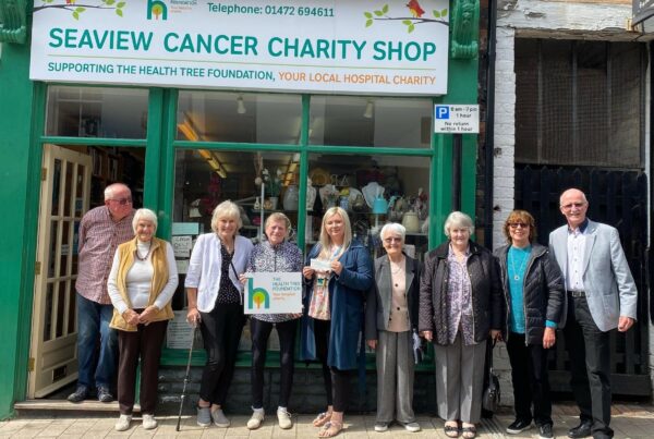 Photo of volunteers standing out side a shop front holding a cheque