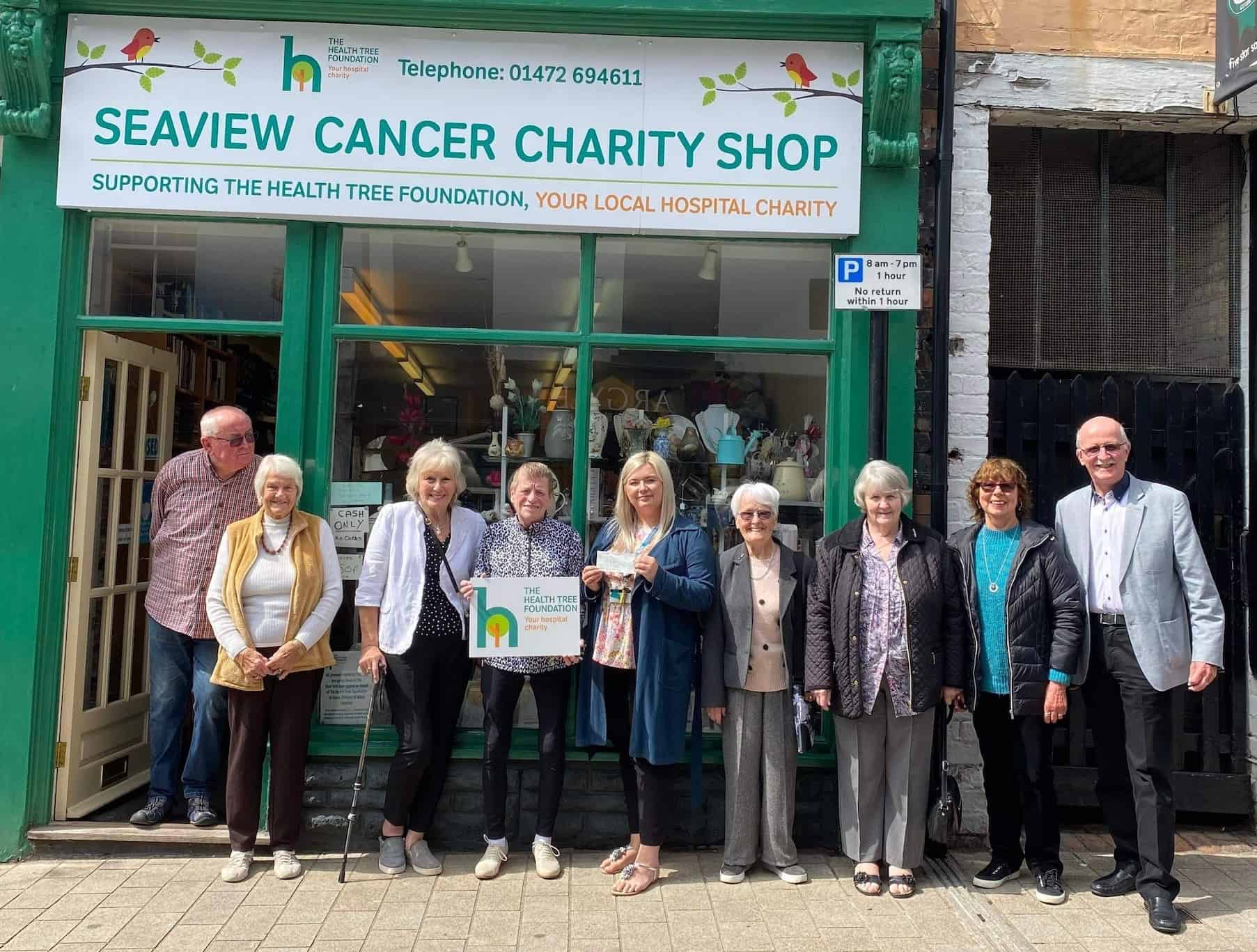 Photo of volunteers standing out side a shop front holding a cheque