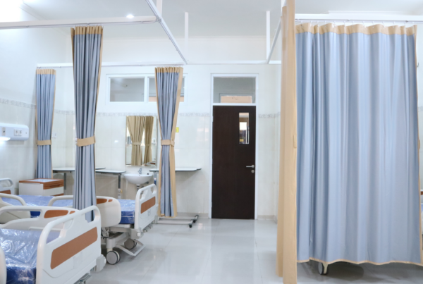 picture of a hospital room bay with a row of beds on the right and a bay on the left with the curtain closed
